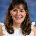 Smiling woman with wavy brown hair, wearing a white top with ruffled sleeves, against a blue backdrop.