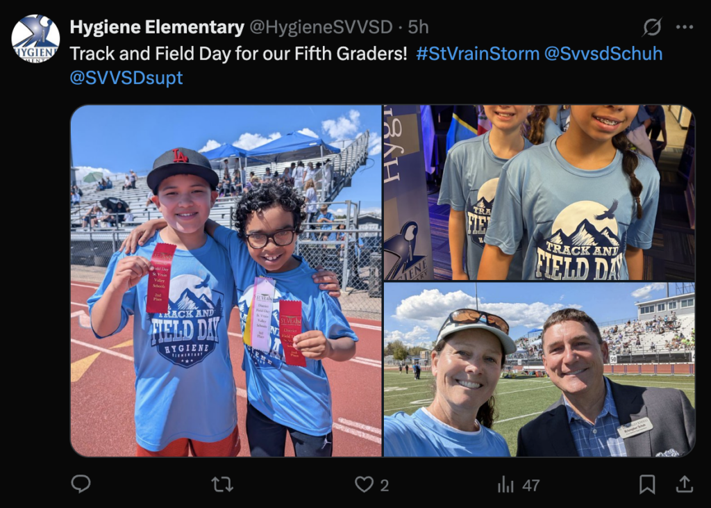 Two students hold ribbons at a track and field day event, with a cheering crowd in the background.