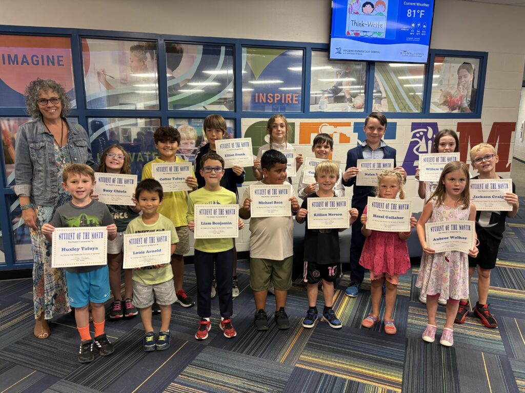 A group of students proudly hold "Student of the Month" certificates, standing with a teacher in a school setting.