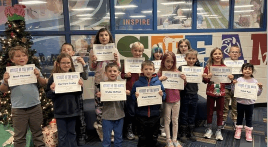 A group of students holding "Student of the Month" certificates stands in front of a decorated Christmas tree.
