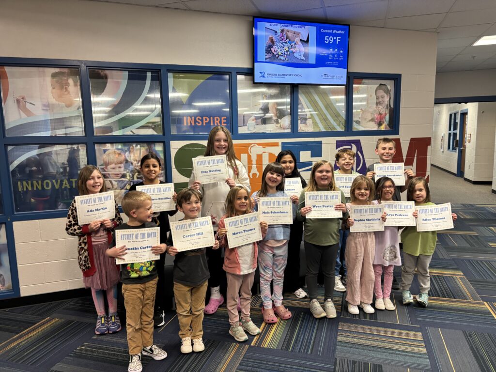 A group of students proudly holding "Student of the Month" certificates in a school hallway.