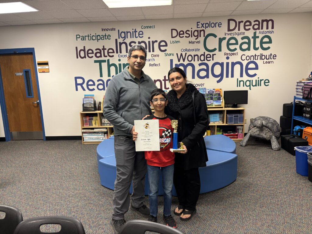 A boy holds a certificate and trophy, flanked by his parents, in a classroom with educational words on the wall.