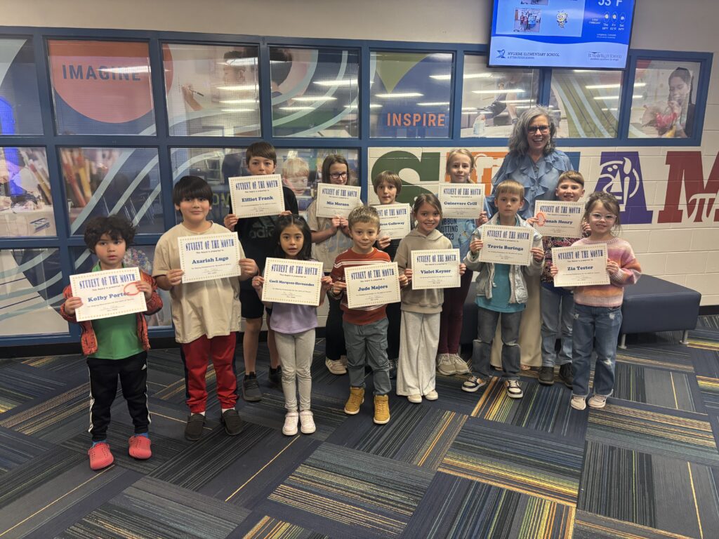 A group of students proudly holding "Student of the Month" certificates, with a teacher standing behind them.