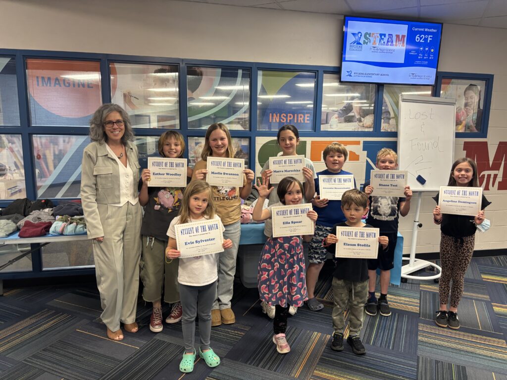 A group of students holds "Student of the Month" certificates with a teacher in a school setting.