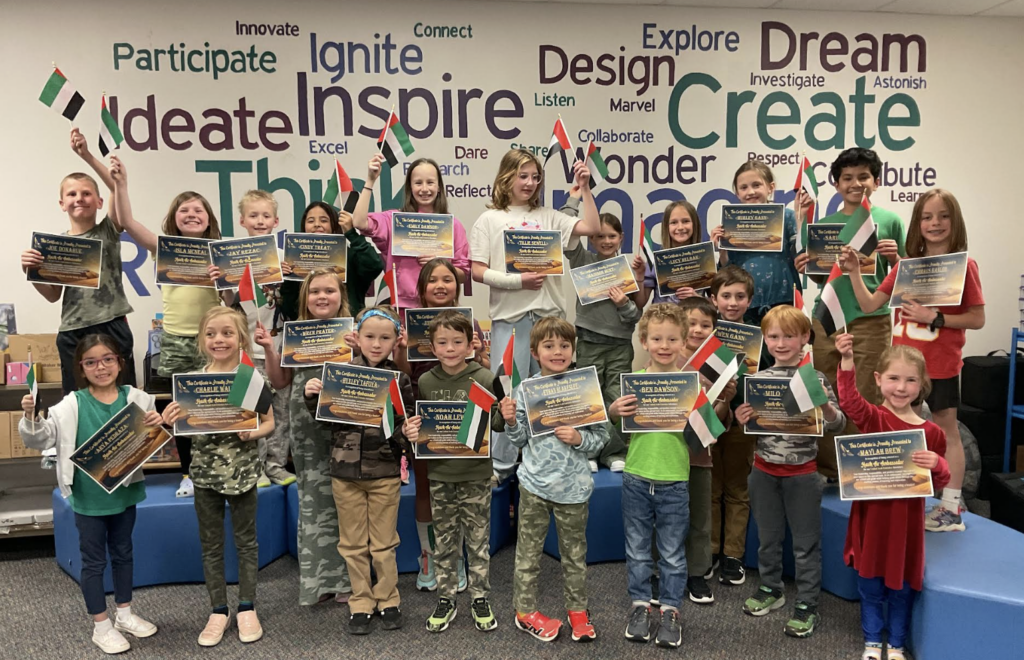 A group of children holding flags and certificates, celebrating an achievement in a classroom setting.