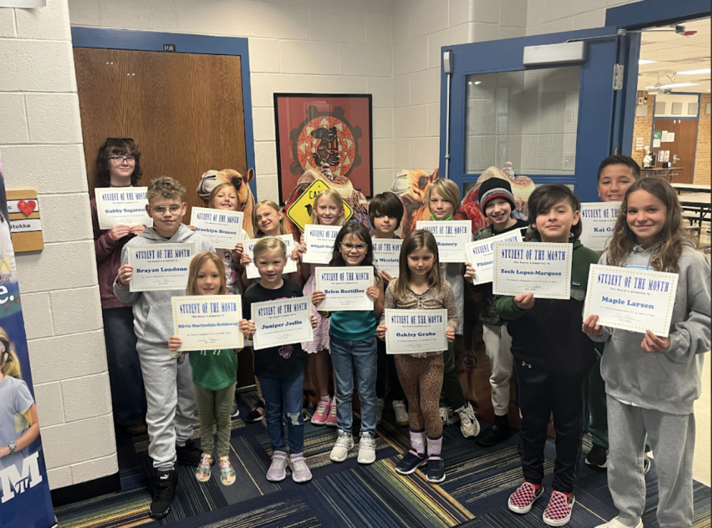 A group of students proudly holding "Student of the Month" certificates in a school hallway.
